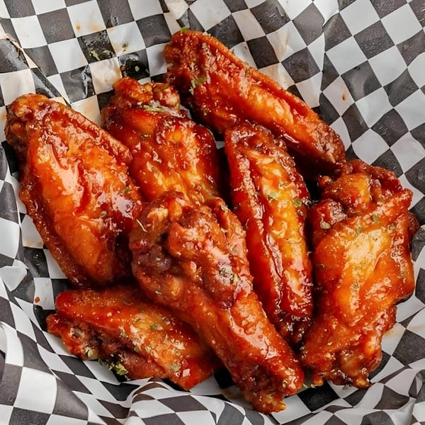Close-up of several glossy, orange-glazed chicken wings with herbs in a black and white checkered paper.