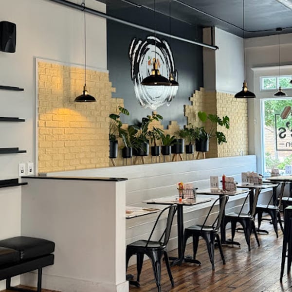 Interior of Mic's Kitchen with black tables, chairs, and a wall with plants and a circular art piece.