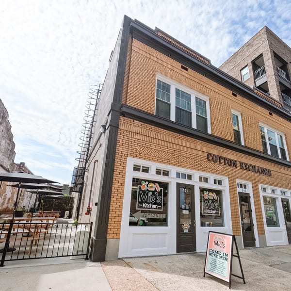 Exterior of Mic's Kitchen, a brick building with a patio featuring picnic tables and umbrellas.